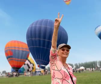 Senior woman who got her wishes granted through Chartwell Wish of a Lifetime poses V hand gesture in front of air balloons / Une aînée dont les vœux ont été exaucés grâce à Chartwell Wish of a Lifetime fait un geste de la main devant des ballons gonflables